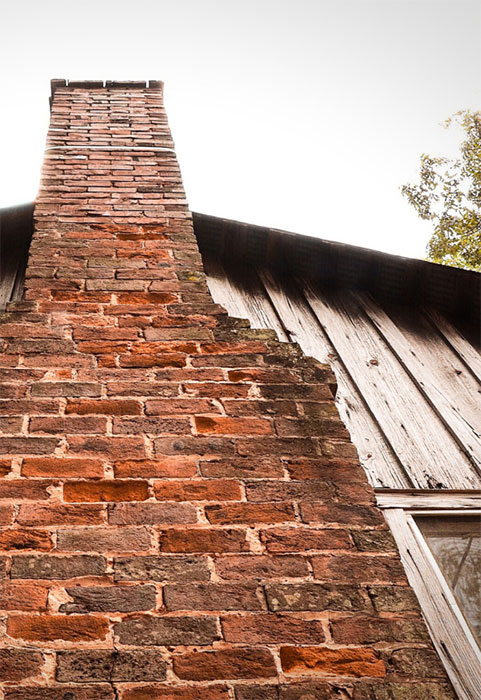 Stock photo of a tall masonry chimney outside of board and batten home.