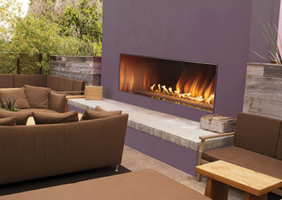 Stock photo of outdoor Linear Gas Fireplace with purple painted surround and limestone hearth. There is also three outdoor sofas.