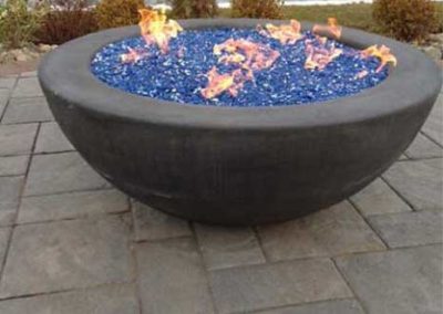 stock photo of bowl fire pit with blue fire glass on patio with lake in the background.