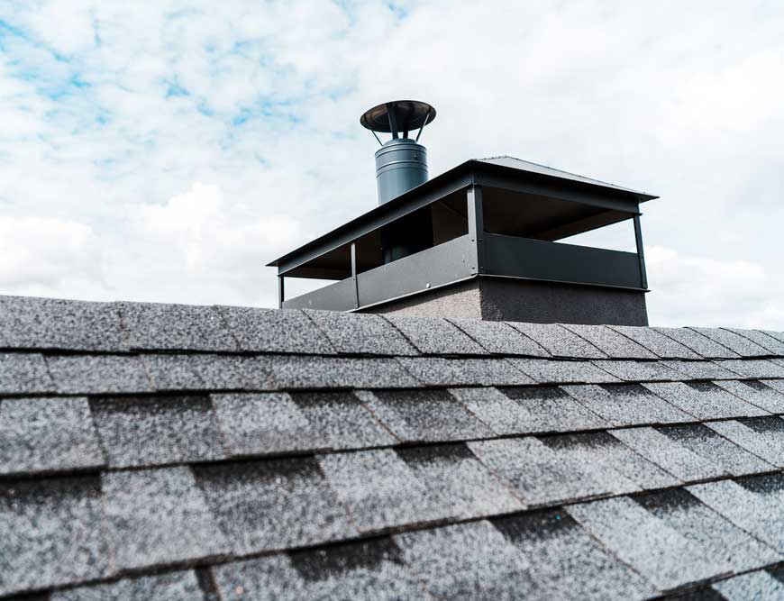 Stock photo of a chimney cap on top of a chimney with clouds in the background.