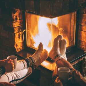 people propping their feet up by a fire while holding cups of a warm beverage